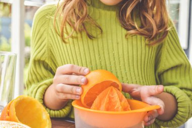 Bir kız çocuğu el sıkacağı ile taze sıkılmış portakal suyu yapar.