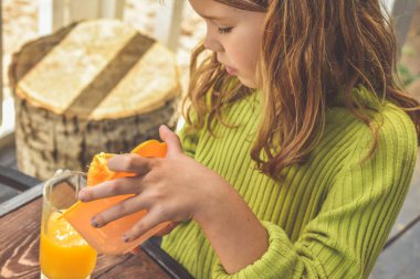 Bir kız çocuğu el sıkacağı ile taze sıkılmış portakal suyu yapar.