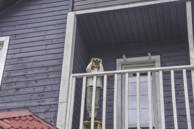 Bir çocuk, evin balkonunda duran dürbünle bakar.