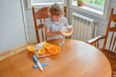 Mutfakta bir kız çocuğu portakal suyunu keser ve sıkar.