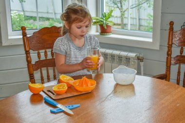Mutfakta bir kız çocuğu portakal suyunu keser ve sıkar.