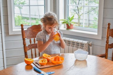 Mutfakta bir kız çocuğu portakal suyunu keser ve sıkar.