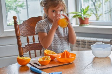 Mutfakta bir kız çocuğu portakal suyunu keser ve sıkar.