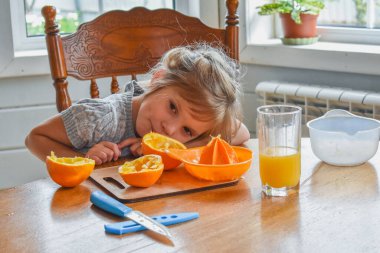 Mutfakta bir kız çocuğu portakal suyunu keser ve sıkar.