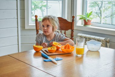 Mutfakta bir kız çocuğu portakal suyunu keser ve sıkar.