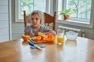 Mutfakta bir kız çocuğu portakal suyunu keser ve sıkar.