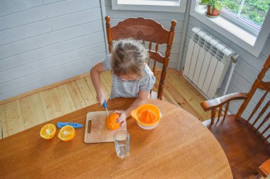 Mutfakta bir kız çocuğu portakal suyunu keser ve sıkar.