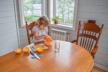 Mutfakta bir kız çocuğu portakal suyunu keser ve sıkar.