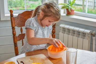 Mutfakta bir kız çocuğu portakal suyunu keser ve sıkar.
