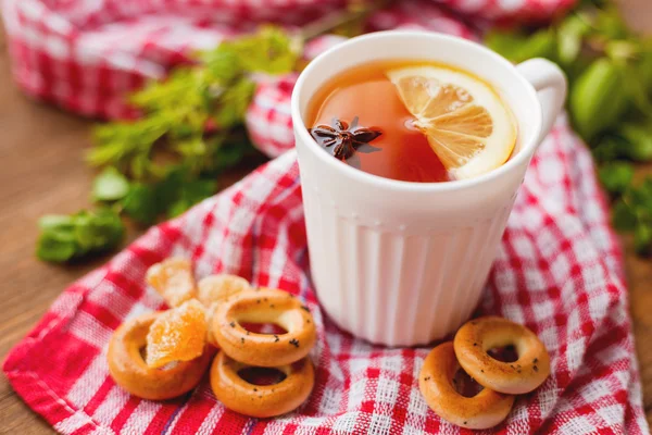 Cup of hot tea with lemon and anise star. White mug with hot beverage on plaid red towel with ginger pieces and cookies. — Stock Photo, Image