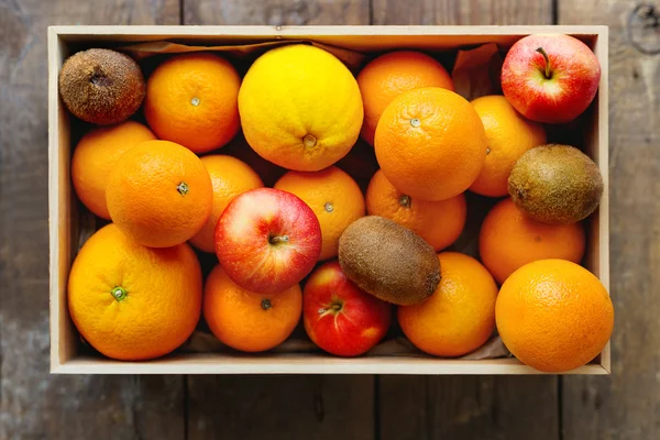 Caixa cheia de frutas frescas. Colheita de fruto - maçãs, laranjas, limão, quivi. Mesa de madeira rústica . — Fotografia de Stock