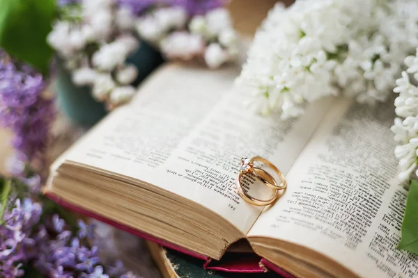 Pair of wedding rings with diamond. Rustic background with old books and lilac flowers. Retro background. — Stock Photo, Image