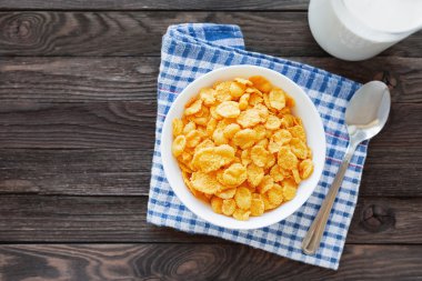 Süt şişesi ile kase lezzetli mısır gevreği. Ekose tartan peçete ile Rustik ahşap arka plan. Sağlıklı gevrek kahvaltı atıştırmalık. Metin için yer. Üst görünüm, düz yatıyordu.
