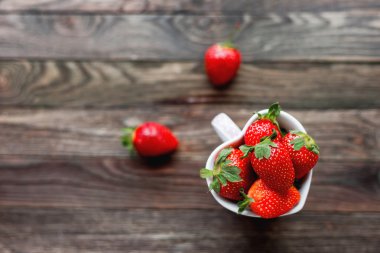 Bir kalp, aşk sembolü biçiminde kap taze sulu çilek. Rustik ahşap arka plan. Üstten Görünüm, metin için yer.