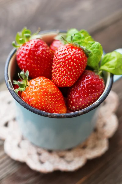 Eski paslı mug içinde taze sulu çilek. Tığ işi peçete ile rustik ahşap arka plan.