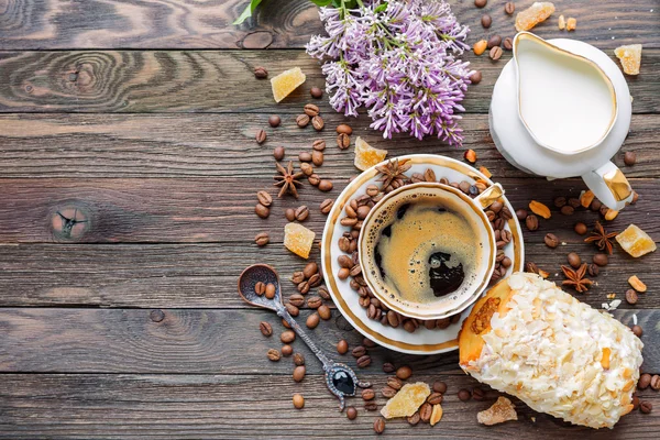 Rustieke houten achtergrond met kopje koffie, melk, broodje met marsepein en lila bloemen — Stockfoto