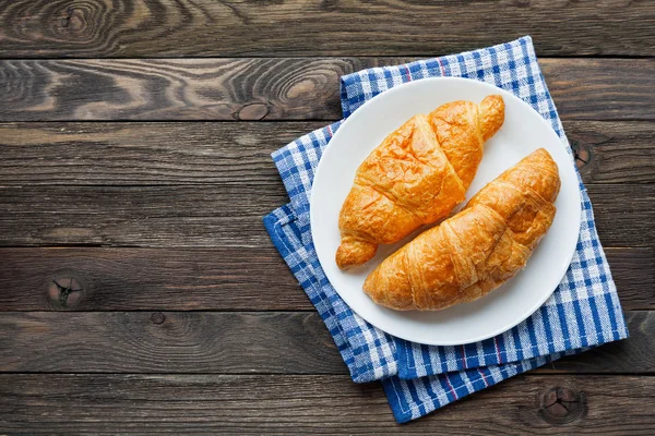 Fondo del desayuno continental - par de croissants en servilleta azul a cuadros. Fondo rústico de madera con lugar para texto. Vista superior . —  Fotos de Stock