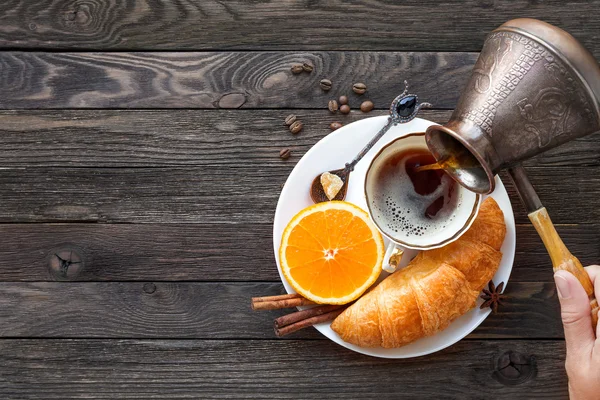 Desayuno continental - cezve y taza de café caliente, croissant y naranja. Sabrosa comida sobre fondo rústico de madera. Vista superior, lugar para el texto . —  Fotos de Stock