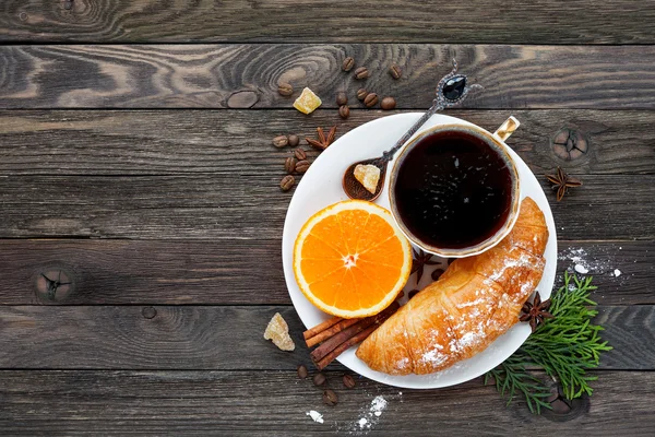 Continentaal ontbijt - kopje warme koffie, croissantje en oranje. Lekker eten op rustieke houten achtergrond. Bovenaanzicht, plaats voor tekst. — Stockfoto