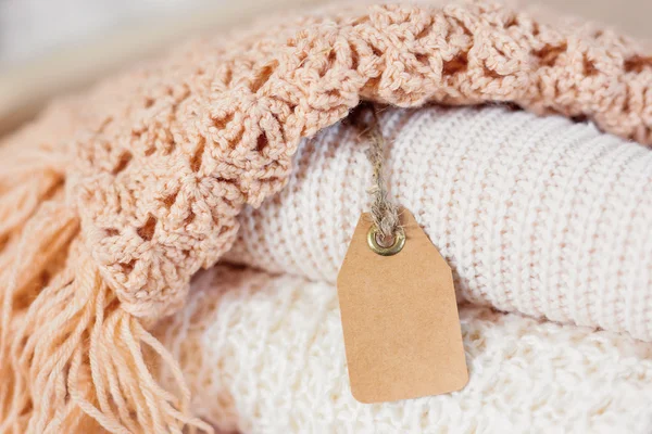 ベージュのニット服の山。かぎ針編みの暖かいマフラーとセーターが 1 つのヒープに折り畳まれています。Clear タグ上のテキストを配置します。. — ストック写真