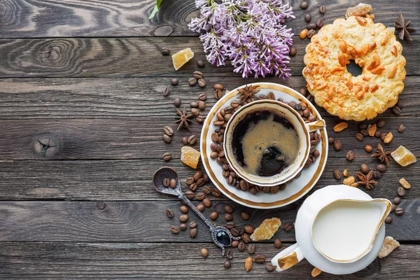 Rustic wooden background with cup of coffee, milk, peanut tart, sugar ginger and lilac flowers. — Stock Photo, Image