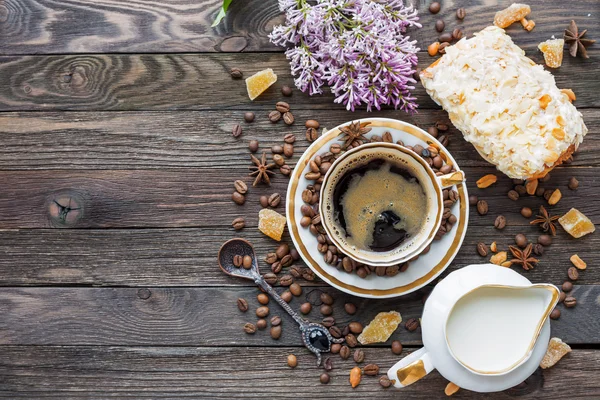 Rustieke houten achtergrond met kopje koffie, melk, broodje met marsepein en lila bloemen. — Stockfoto