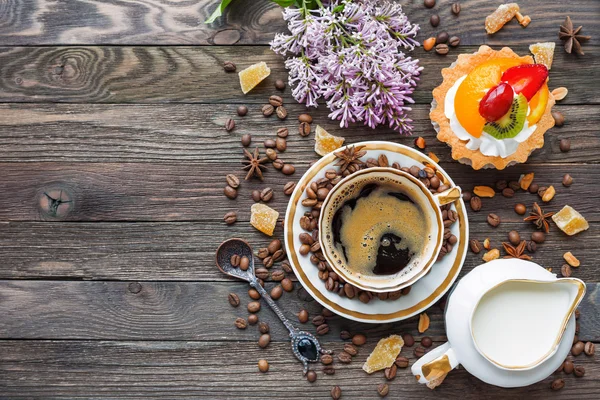 Rustic wooden background with cup of coffee, milk, fruit tart and lilac flowers. — Stock Photo, Image