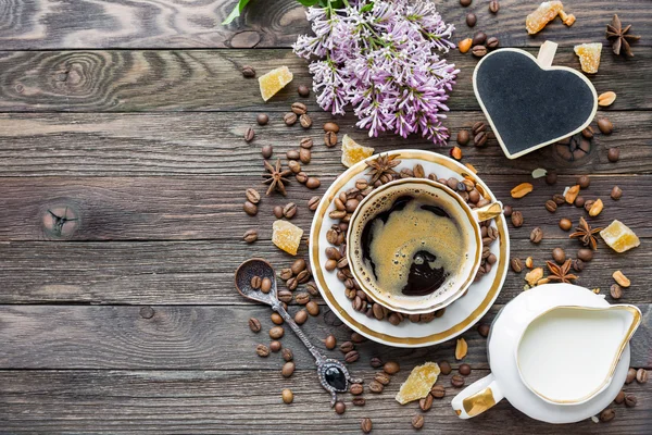 Rustieke houten achtergrond met kopje koffie, melk, suiker gember en lila bloemen. — Stockfoto