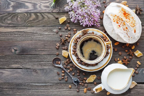 Rustieke houten achtergrond met kopje koffie, melk, meringue met pinda's en lila bloemen. — Stockfoto