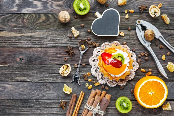 Fondo rústico de madera con tarta de frutas, especias, kiwi y naranjas. Tiza de corazón para text.Top vista, plano laico . —  Fotos de Stock