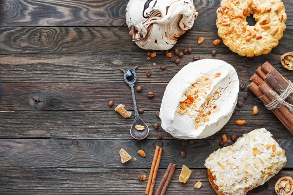 Rustic wooden background with different pastries - chocolate and peanut meringue, tart, marzipan bun. — Stock Photo, Image