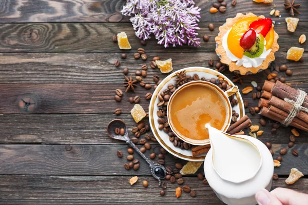 Rustic wooden background with cup of coffee, milk, fruit tart and lilac flowers. — Stock Photo, Image