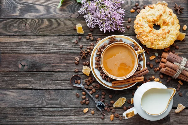 Rustic wooden background with cup of coffee, milk, peanut tart, sugar ginger and lilac flowers. — Stock Photo, Image