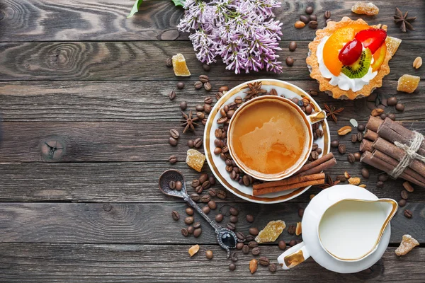 Rustieke houten achtergrond met kopje koffie, melk, vruchten taart en lila bloemen. — Stockfoto