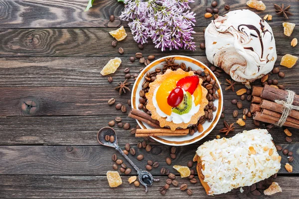 Rustic wooden background with different pastries - chocolate meringue, fruit tart, marzipan bun. — Stock Photo, Image