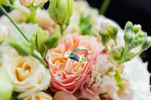 Anillos de oro con diamantes se encuentran dentro de la flor de rosa en ramo de novia. Símbolo de amor y matrimonio . — Foto de Stock