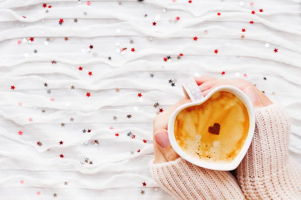 Mulher segura uma xícara de café quente com coração de canela. Inverno e Dia dos Namorados tecido fundo com prata espumante e confete vermelho . — Fotografia de Stock