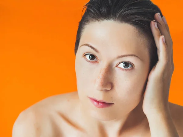Portrait of woman with freckles on orange monochrome background. No make up. Natural beauty on bright and colorful backdrop. Banner with copy space.