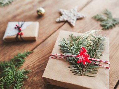 Noel hediyeleri ağaç dallarıyla sarılı el işi kağıtları. Noel ağacı şeklinde kırmızı süslemeler, yıldızlar. Ahşap arka planda yeni yıl hediyeleri. Kış tatili ruhu.