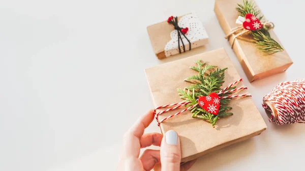 Christmas DIY presents wrapped in craft paper with fir tree twigs and red hearts. Top view on decorations on New Year gifts. Festive background. Winter holiday spirit. Banner with copy space.