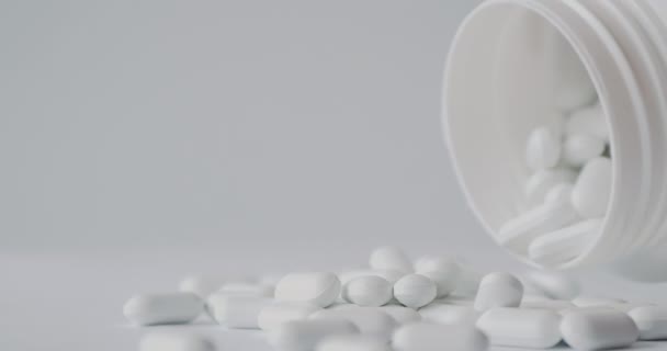 Bílé pilulky se vysypaly z plastové nádoby. Léky kapsle na bílém pozadí. — Stock video