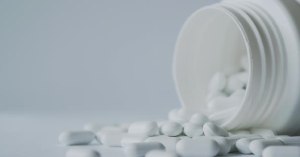 Λευκά χάπια χύθηκαν από ένα πλαστικό βάζο. Κάψουλες φαρμάκων σε λευκό φόντο. — Αρχείο Βίντεο
