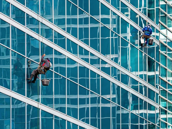 Two industrial climbers with safety tethers wash the glass walls of modern skyscraper. Dangerous work in the metropolis.