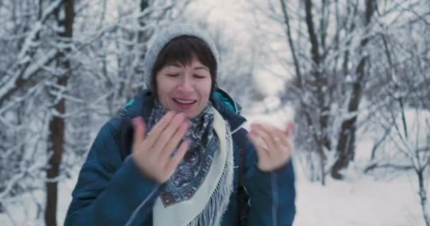 女性は雪の多い冬の森の中で冷たい手を息で温めます。女は木の間を歩くと笑う。誠実な感情. — ストック動画