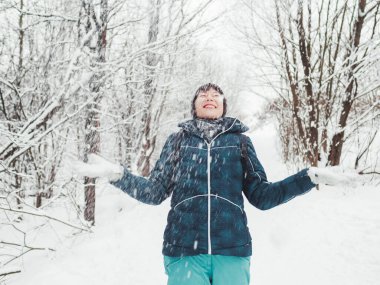 Gülen kadın karla oynuyor. Karlı kış ormanlarında eğlence. Kadın ağaçların arasında yürürken gülüyor. Samimi duygular.