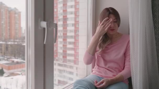 Vrouw met krullend haar en roze longsleeve zit op vensterbank. — Stockvideo