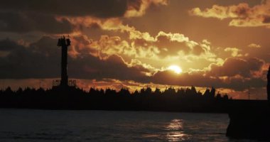 Martılar ve karabataklar dalgakıranların üzerinde otururlar. Muhteşem günbatımı arka planında deniz feneri. Soçi Limanı, Rusya.