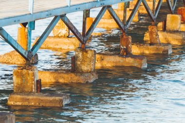 Kızıl Deniz 'in üzerindeki ahşap iskelelerin beton üsleri. Mavi su yüzeyinde gün batımı ışığı. Renkli yapı.