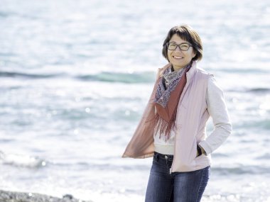 Deniz kenarında yürüyen gülümseyen kadın. Okyanus kıyısında tatil. Kadının arkasında mutlu bir gülümsemeyle turkuaz su..