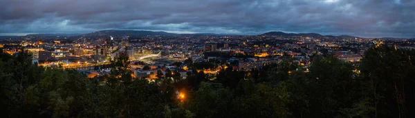 Night panoramic view of Oslo, capital of Norway. Dark cloudscape ower capital of Norway. Scandinavian city with lighted buildings and bridges, surrounded by forests.